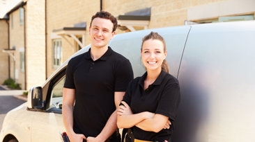 A cheerful man and woman smiling in front of a van