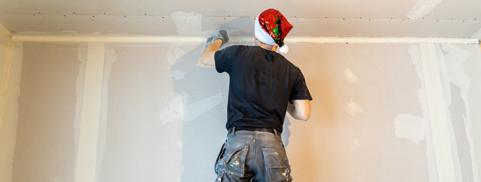 Professional painter in Santa hat applying plaster